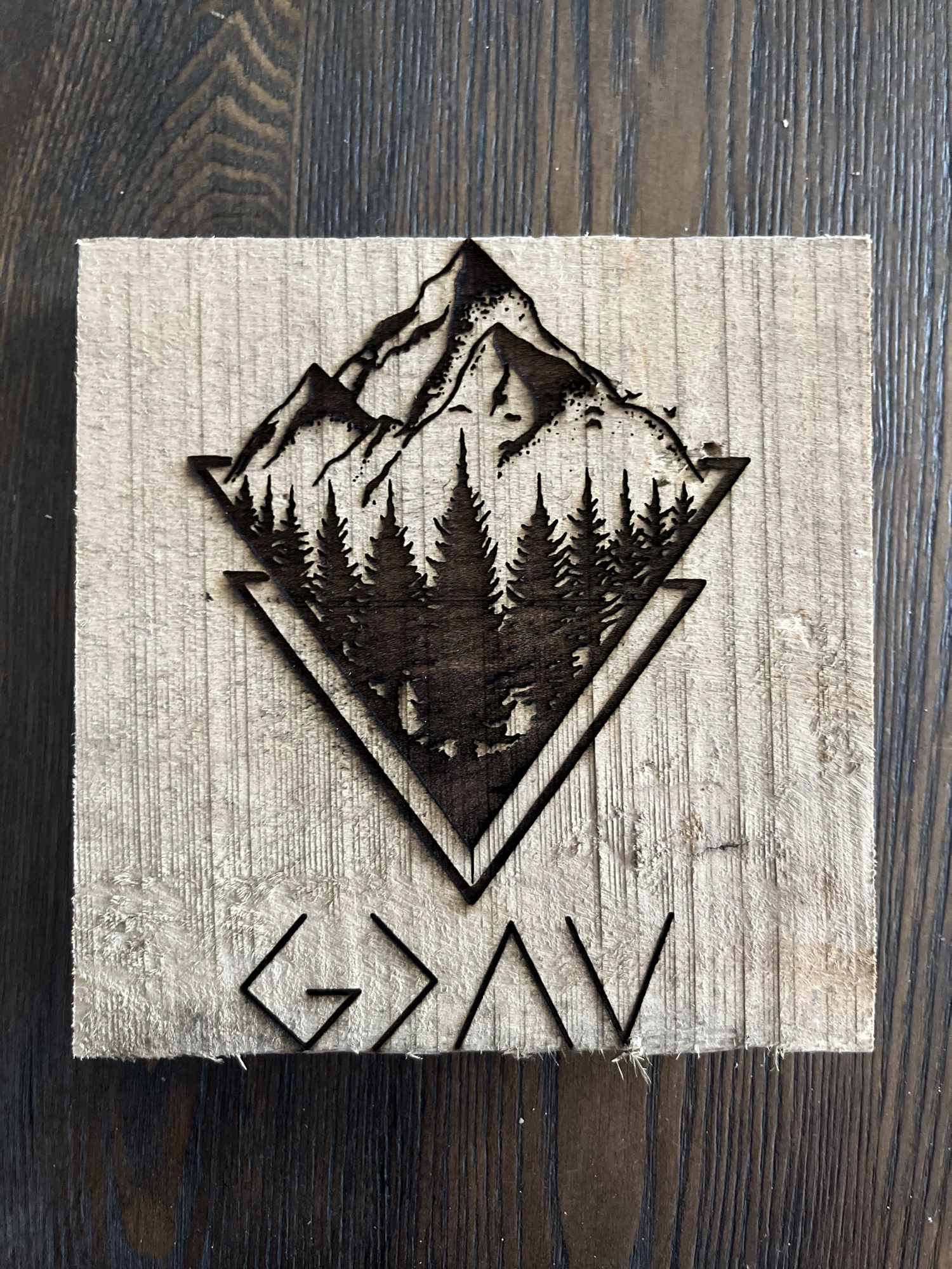 Laser-engraved wood block depicting a mountain and forest scene